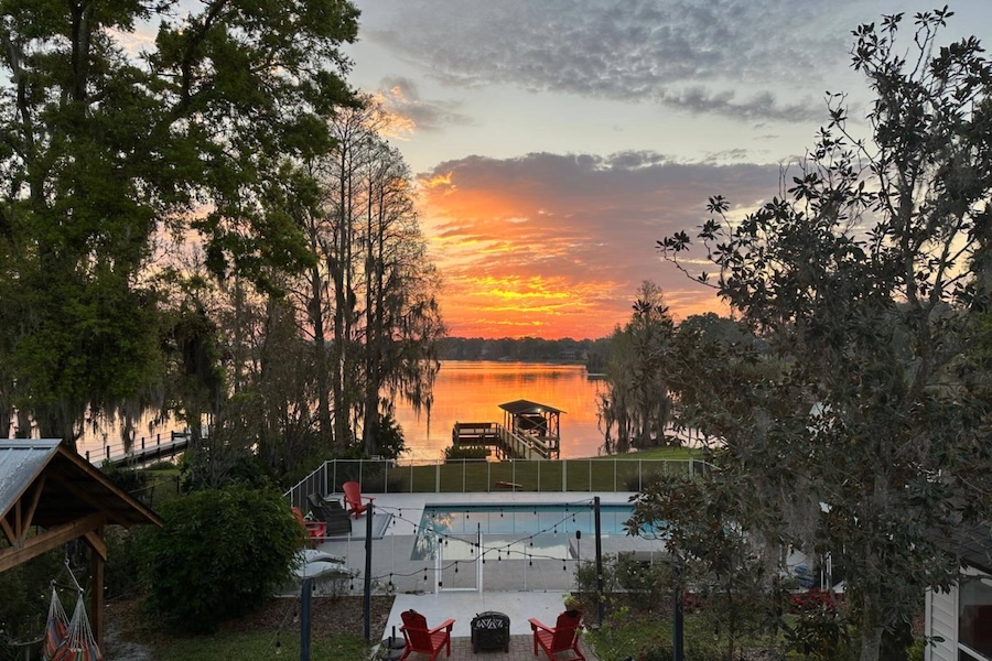 Photo of a sunset with orange in the sky over Lake Otis water and a pool with a dock by the lake
