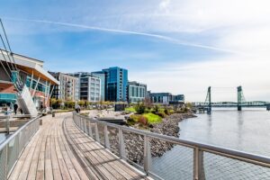 Photo of a boardwalk along a river with buildings in the background