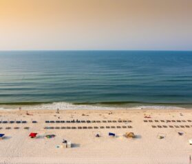 Aerial photo of a sunrise on the Gulf Shores of Alabama, spotted with rows of chairs and a few beachgoers