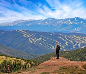 Photo of a hiker overlooking the trails of Keystone, Colorado and mountains in the distance with trees