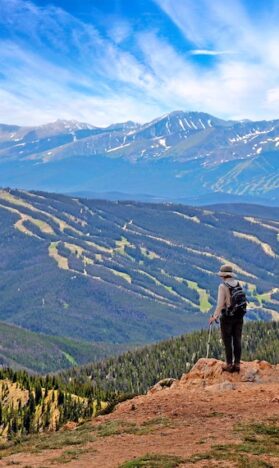Photo of a hiker overlooking the trails of Keystone, Colorado and mountains in the distance with trees