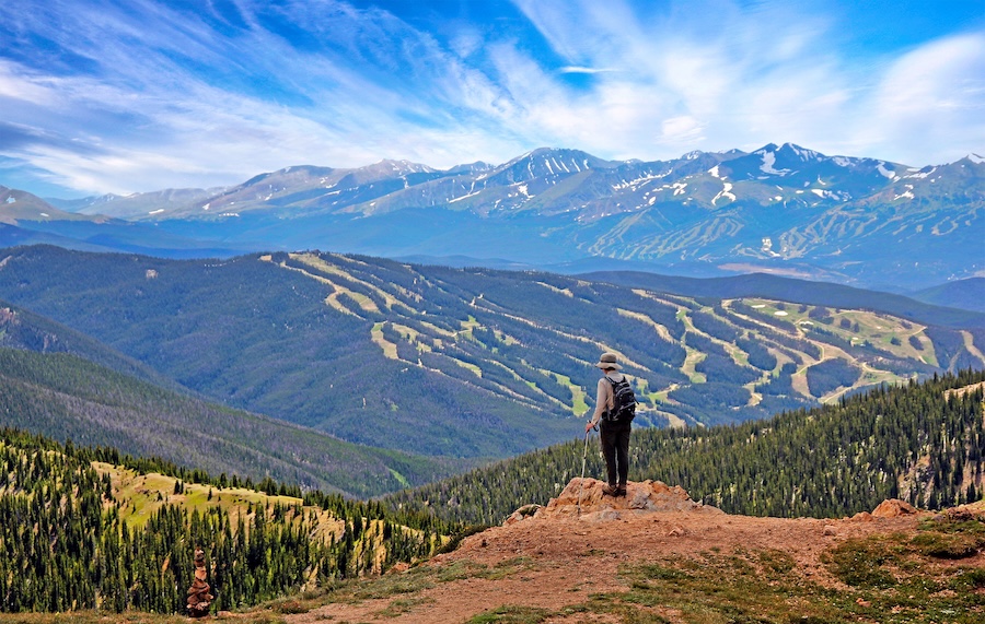 Photo of a hiker overlooking the trails of Keystone, Colorado and mountains in the distance with trees