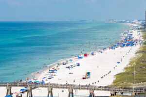 Aerial photo of the white sand beach and bright blue waters of PCB, spotted with sunbathers and umbrellas