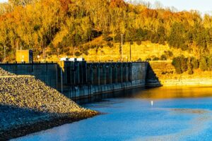 Photo of the dam at Center Hill lake, with trees on the land in the distance with fall color leaves