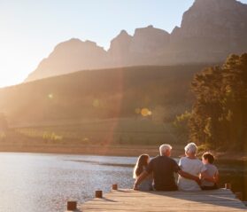 Multi-generational family enjoying sunset together by a lake, illustrating large family vacation homes for multi-gen travel and quality time outdoors.