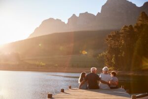 Multi-generational family enjoying sunset together by a lake, illustrating large family vacation homes for multi-gen travel and quality time outdoors.